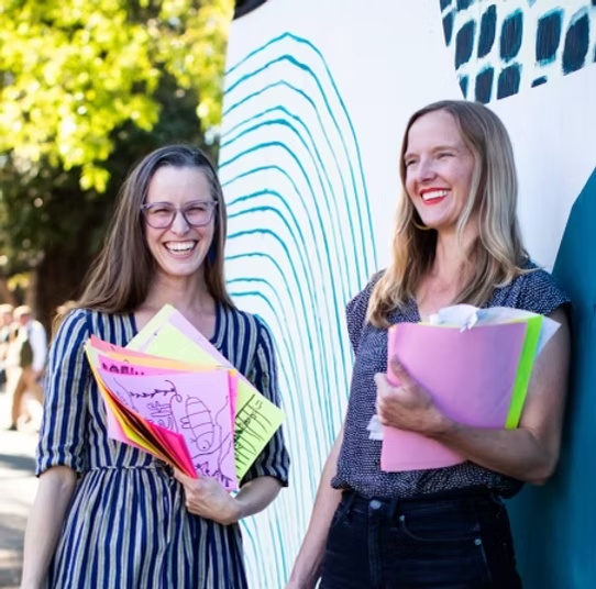 Two people holding colorful artwork in the photograph on Peptoc’s Our Story page.